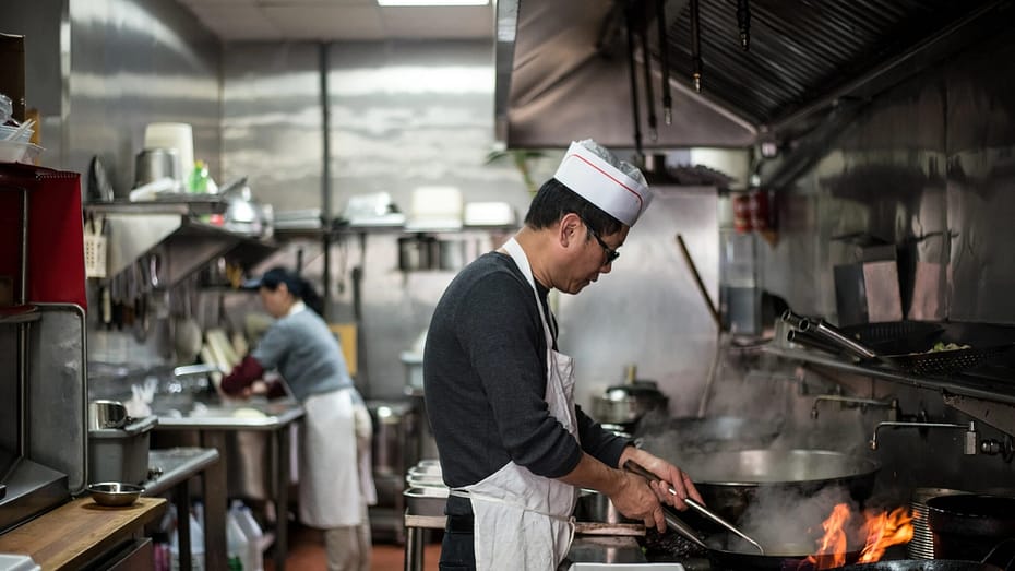 A cook named Mr. Chen mans the wok in the kitchen at Happy Wok in Crown Heights, USA.