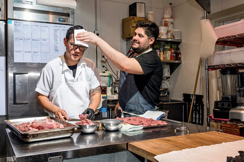Two checks working, prepping lots of meat. The one on the right, bearded is mopping the brow of the other with a small white cloth. The other chef has glasses and carries on with his knife work. For Stone and von Hauske, it’s all about supporting each other.